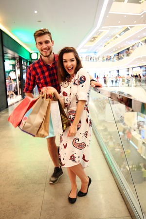 sale, consumerism and people concept - happy young couple with shopping bags walking in mall.の写真素材
