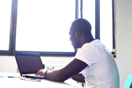 Full concentration. Close-up part of young African man using laptop while sitting at his working placeの写真素材