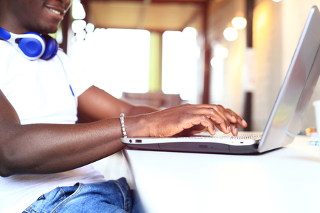 Full concentration. Close-up part of young African man using laptop while sitting at his working placeの写真素材