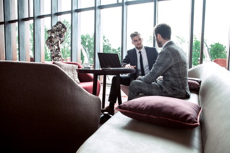 Image of two young businessmen using touchpad at meeting.の写真素材