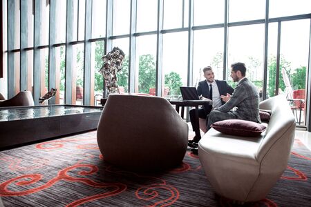 Image of two young businessmen using touchpad at meeting.