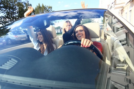 three girls driving in a convertible car and having fun.