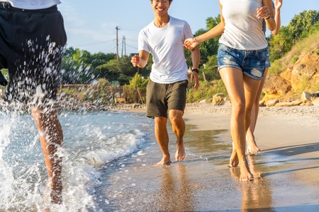 Group Of Friends Run Through Waves Together On Beach Vacation.の写真素材