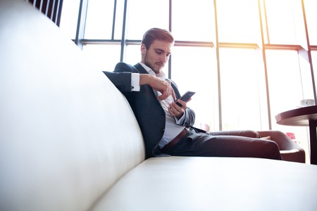 Portrait of happy young businessman sitting on sofa in hotel lobby.の写真素材