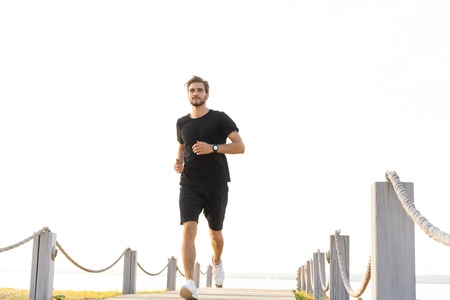 Full length shot of healthy young man running on the promenade. Male runner sprinting outdoors
