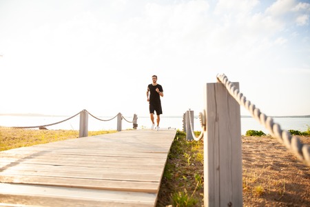 Full length shot of healthy young man running on the promenade. Male runner sprinting outdoors