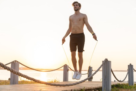Portrait of muscular young man exercising with jumping rope
