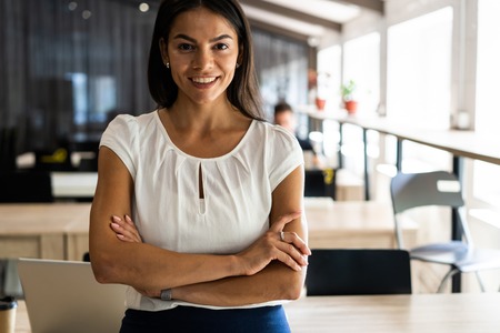 Smiling professional businesswoman in casual, with arms crossed standing in office.の写真素材