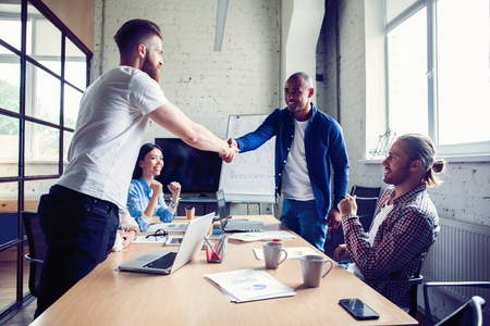New business partners. Young modern colleagues in smart casual wear shaking hands and smiling while sitting in the creative office.の写真素材