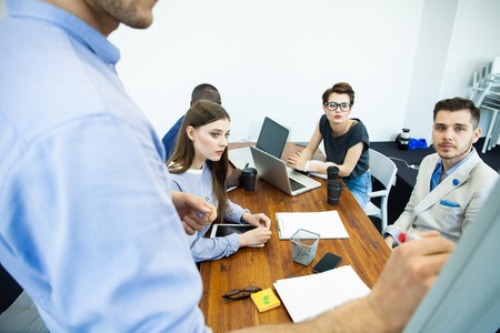 Discussing company progress. Confident young man standing near whiteboard and pointing graph while...