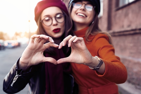 Outdoors fashion portrait young pretty best girls friends in friendly hug. Walking at the city. Posing at the street. Wearing stylish outerwear and hats. Bright make up. Positive emotions.の写真素材