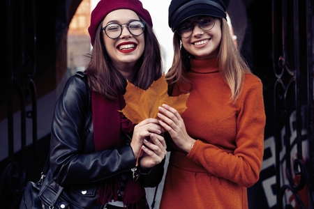 Outdoors fashion portrait young pretty best girls friends in friendly hug. Walking at the city. Posing at the street. Wearing stylish outerwear and hats. Bright make up. Positive emotions.の写真素材