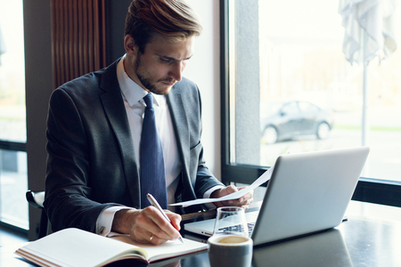 Attractive businessman using a laptop and smiling while working in cafeの写真素材