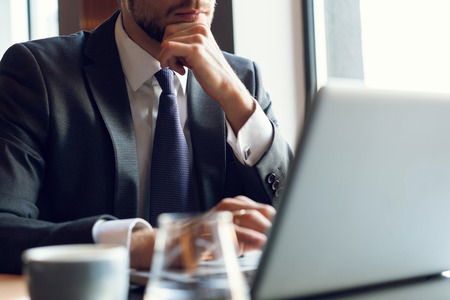 Attractive businessman using a laptop and smiling while working in cafeの写真素材