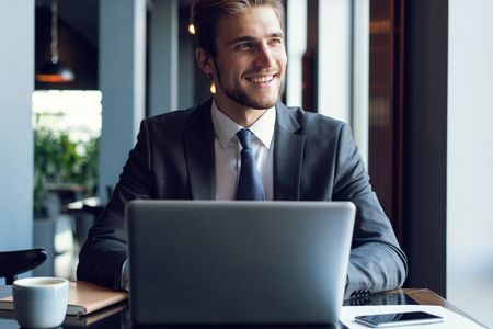 Attractive businessman using a laptop and smiling while working in cafeの写真素材