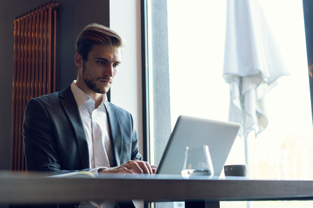Attractive businessman using a laptop and smiling while working in cafeの写真素材