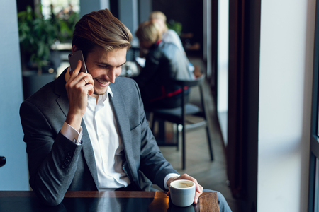Handsome businessman talking on the phone during coffee break in a cafe.の写真素材