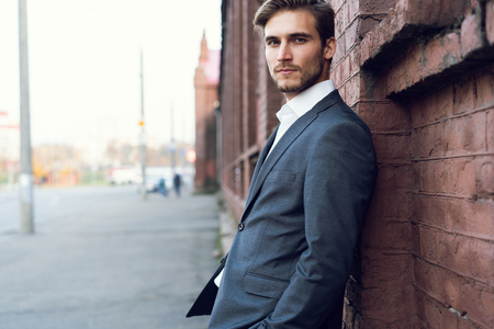 Smiling young male manager formal dressed leaning on a wall outdoors.の写真素材