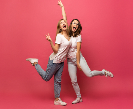Two exited woman having fun and raising hands up. Standing on pink background. Lucky mood.の写真素材