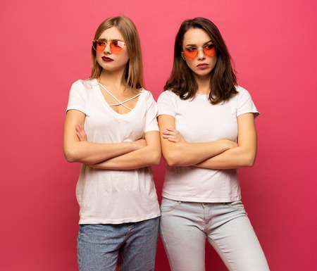 angry young two ladies standing over pink backgroundの写真素材