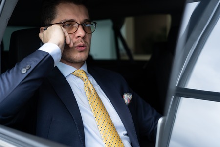 Young businessman sitting on back seat of the car, while his chauffeur is driving automobile.の写真素材
