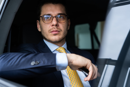 Young businessman sitting on back seat of the car, while his chauffeur is driving automobile.の写真素材