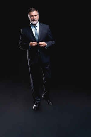 Full length portrait of Mature business man wearing formal suit standing on black background.の写真素材