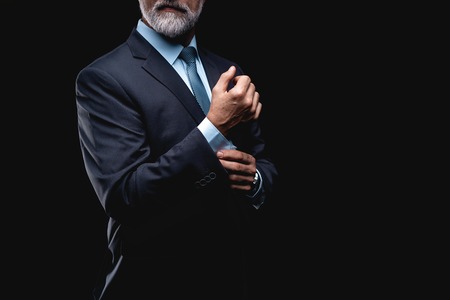 elegant mature fashion man looking at his cufflinks while fixing them.の写真素材