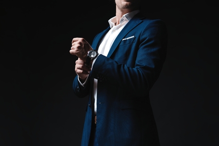 Perfect to the last detail. Handsome young businessman adjusting his sleeves while standing against black background.の写真素材