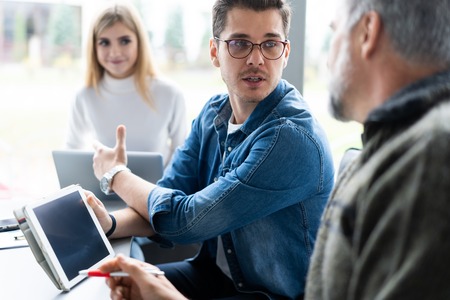 Working day. Group of young modern people in smart casual wear discussing business while working in...