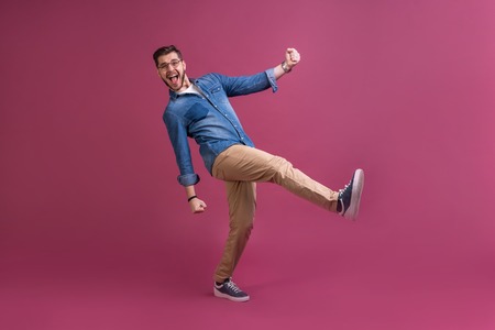 Funny man in casual is having some fun. He is posing and dancing. Isolated on pink background.