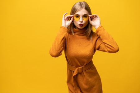 Excited young woman in orange dress, widely smiling, looking at camera. Isolated on yellow backgroundの写真素材