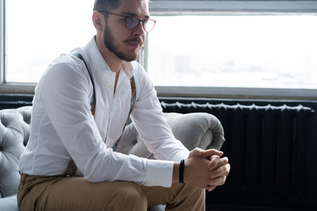 Enjoying free time. Thoughtful young man in full suit looking away while sitting on the sofa at home.の写真素材