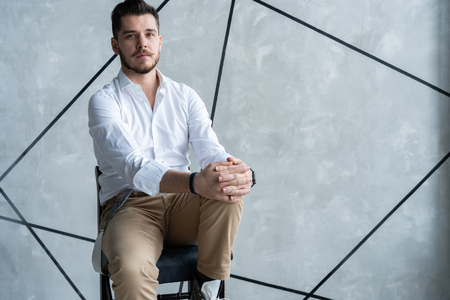 Full length of thoughtful young man in full suit looking away while sitting on the stool.の写真素材