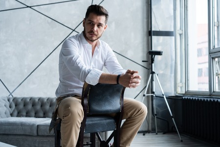 Full length of thoughtful young man in full suit looking away while sitting on the stool.の写真素材