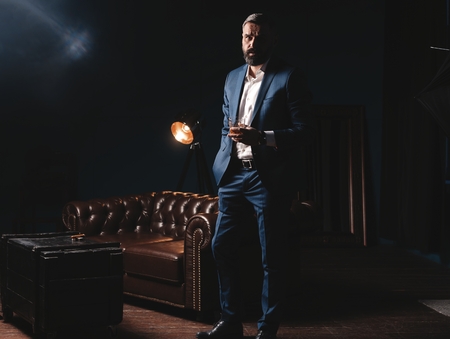 Degustation, tasting. Man with beard holds glass of brandy. Tasting and degustation concept. Bearded businessman in elegant suit with glass of whiskeyの写真素材