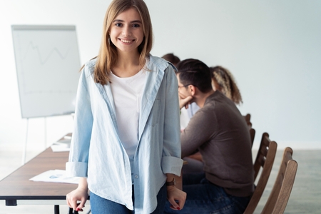 Beautiful young business lady looking at camera and smiling while her colleagues working in the background.の写真素材