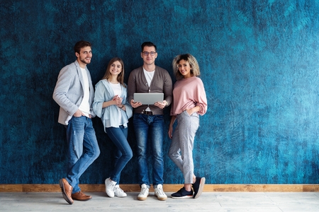 The connected team is an efficient team. Group of businesspeople using wireless technology together while standing in line against a blue background.の写真素材