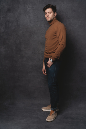 Handsome young man on gray background looking at camera. Portrait of young man with hands in pockets leaning against gray wall.の写真素材