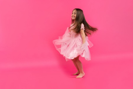 Cute little girl dreams of becoming a ballerina. Little Dancing Girl. Studio Shoot Over Pink Backgroundの写真素材