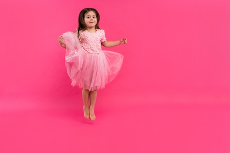 Cute little girl dreams of becoming a ballerina. Little Dancing Girl. Studio Shoot Over Pink Backgroundの写真素材