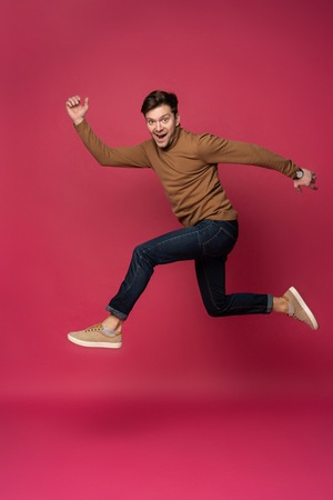 Happy excited cheerful young man jumping and celebrating success isolated on a pink background.の写真素材