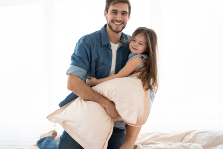 happy father and daughter playing pillow fight in bed at morningの写真素材