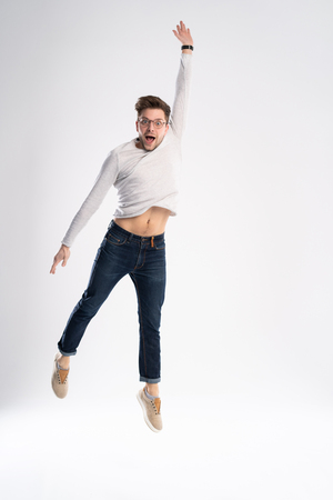 Full-length photo of funny man 30s in casual t-shirt and jeans jumping isolated over white background.の写真素材