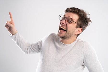 Portrait of young Caucasian guy enjoys funny story or joke, laughs joyfully, has toothy smile, wears white t shirt in one tone with background. Happiness and youth concept.の写真素材