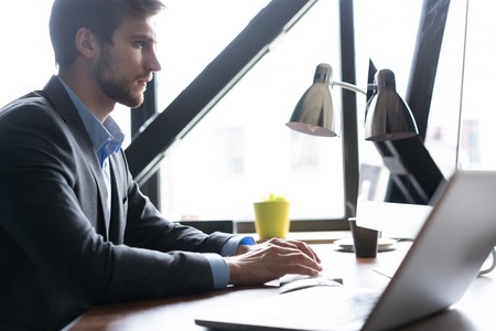 Happy young businessman using laptop at his office desk.の写真素材