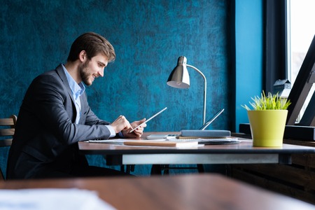 Smiling man in office working on digital tablet.の写真素材