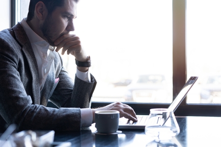 Full concentration. Good looking young man in full suit using computer while sitting in the cafe
