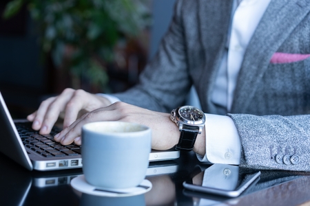 Young man working on his laptop in a coffee shop, rear view of business man hands busy using laptop at office desk.の写真素材