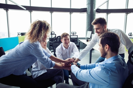 Businesspeople putting their hands on top of each other in nice light workstation, wearing casual...